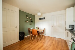 Uma área de refeições compacta com uma mesa redonda, quatro cadeiras, um letreiro com o cardápio de café e um micro-ondas em uma bancada.