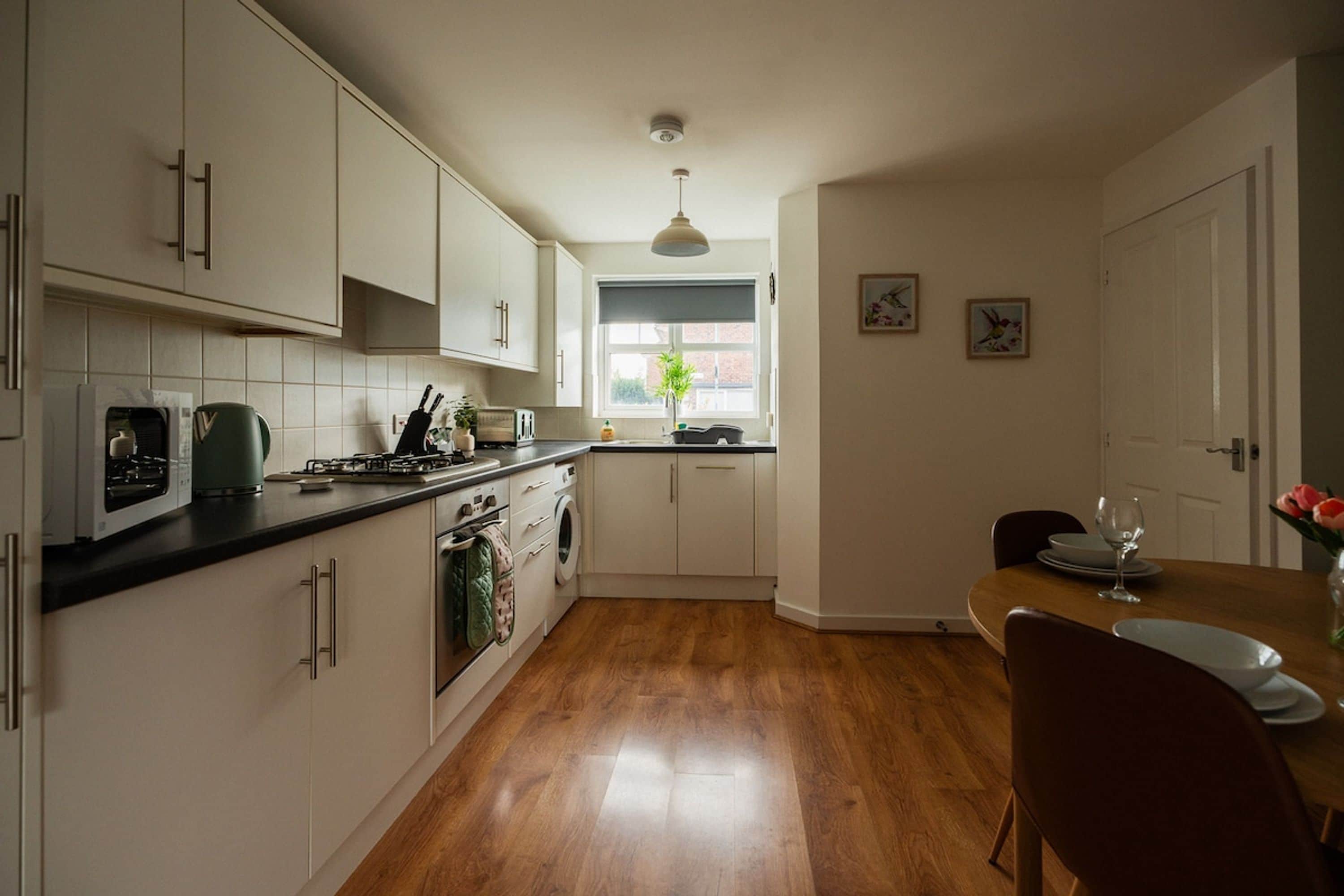 A kitchen with white cabinets, a black countertop, a window with a view, and a dining area with a table and chairs.