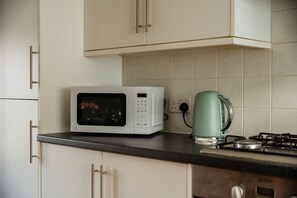 A kitchen with white cabinets, a microwave, a kettle, and a stove. - Einstein House Horizon Stays (Stockton-on-Tees)