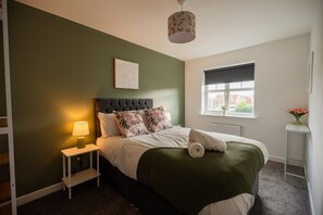 A bedroom with a bed, a nightstand, a lamp, a window, and a wall-mounted picture. - Einstein House Horizon Stays (Stockton-on-Tees)