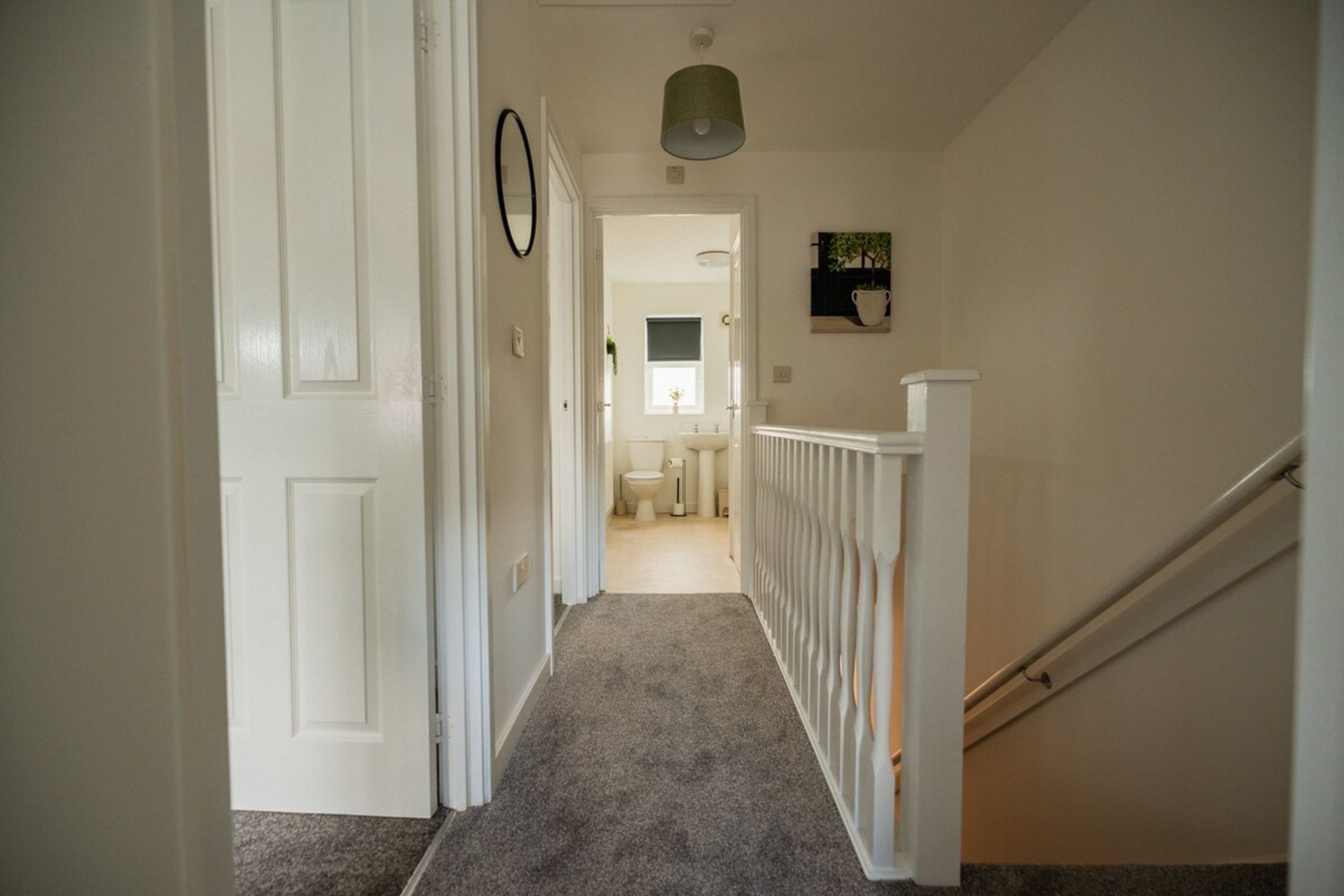 A hallway leading to a bathroom with a toilet, sink, and window.