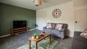 Una sala de estar con un sofá, una mesa de centro con plantas, un televisor y un reloj de pared.