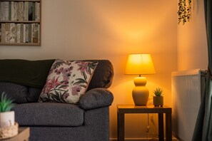 Uma sala de estar aconchegante com um sofá, uma mesa lateral com abajur, um radiador e uma estante.