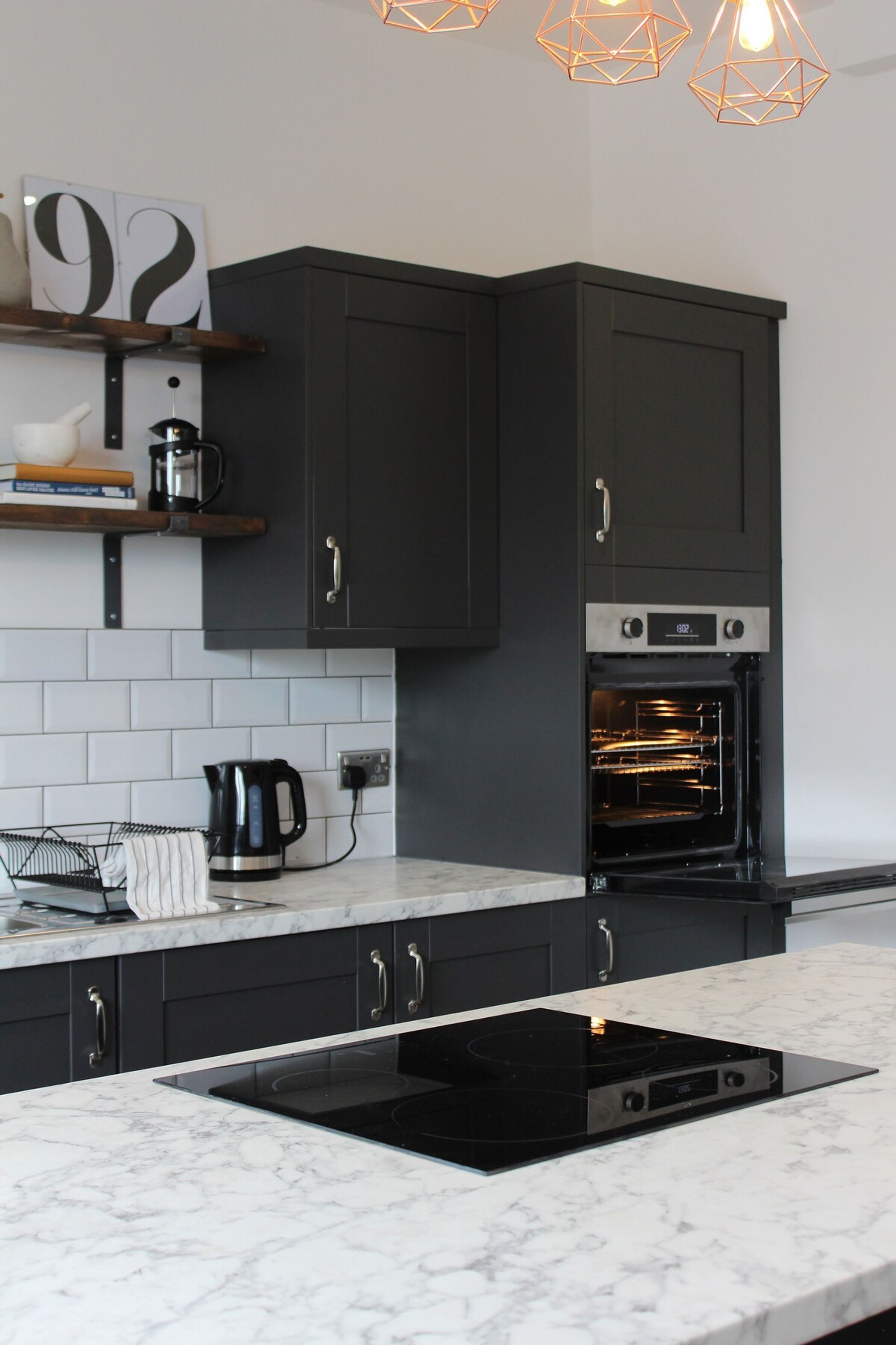 A modern kitchen with dark cabinets, a built-in oven, a black induction cooktop, and a white tiled backsplash.