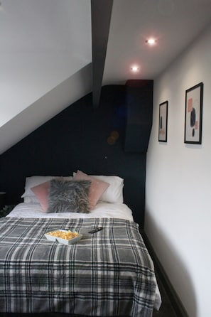 Ein Schlafzimmer mit einem Bett, einer Decke, Kissen, einer Fernbedienung und einer Schale mit Snacks.