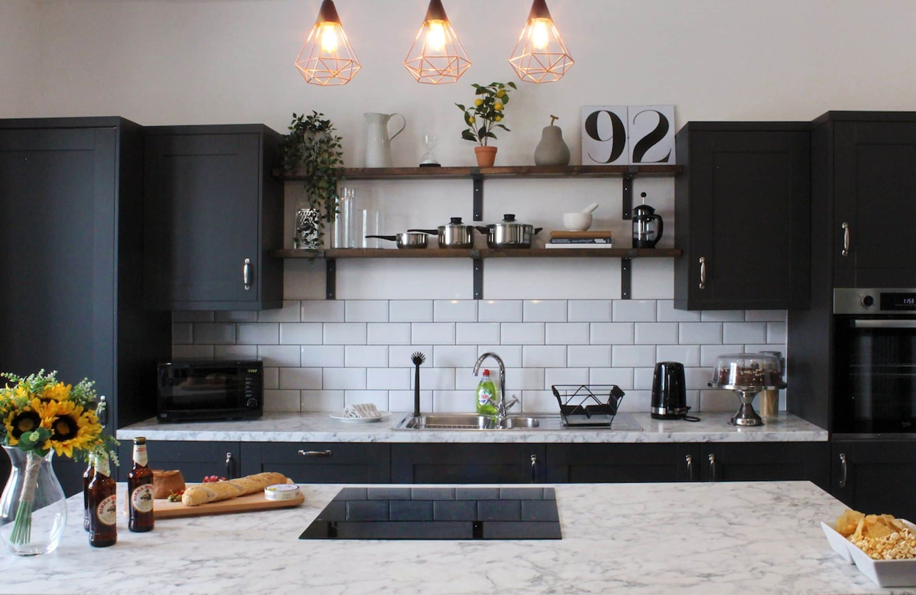 A modern kitchen with dark cabinets, white subway tiles, and a marble countertop.