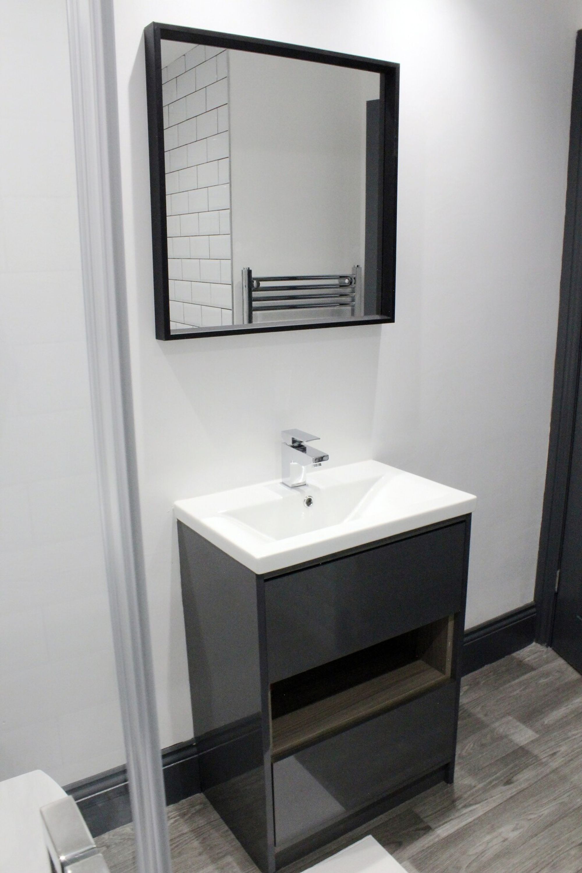 A modern bathroom with a white sink, a mirror, and a towel rack.
