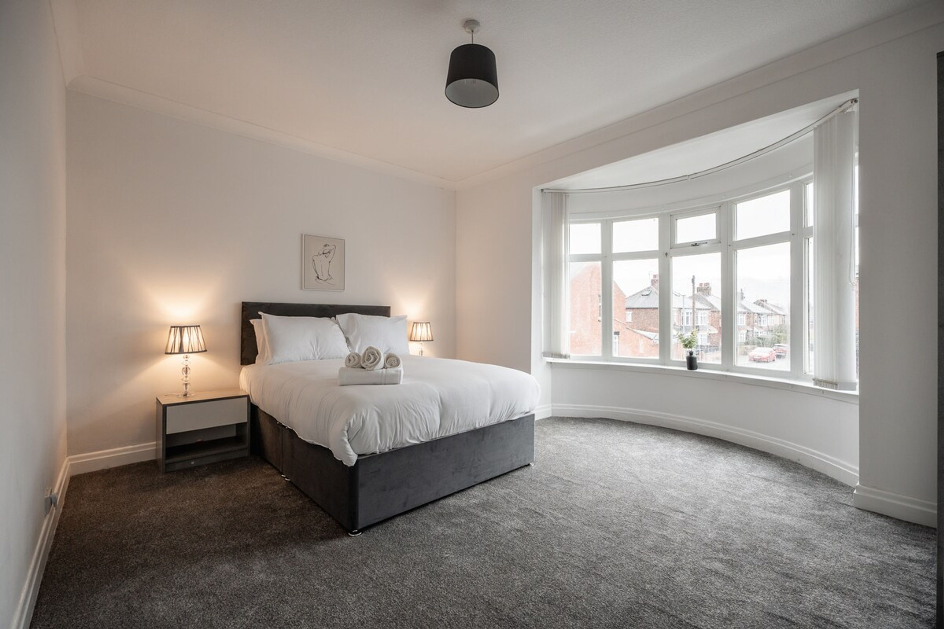 Ein Schlafzimmer mit einem Bett, zwei Nachttischlampen, einem Fenster mit Blick und einer Deckenleuchte.