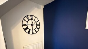 A dining area with a round table, white plates, a potted plant, and a wall clock. - Rochester House Horizon Stays (Middlesbrough)