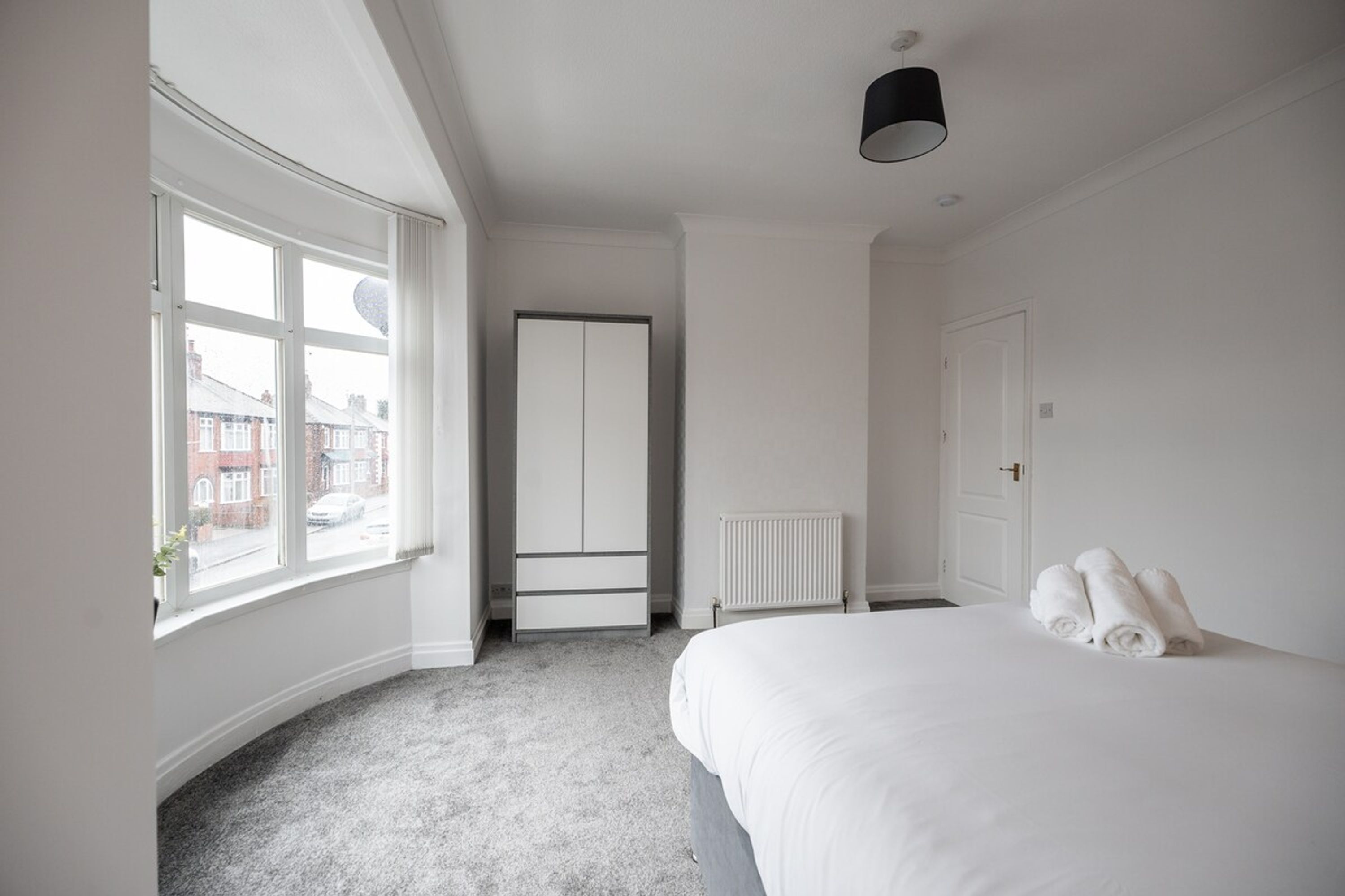 A hotel room with a large bed, a radiator, a wardrobe, and a window with a view of the street.
