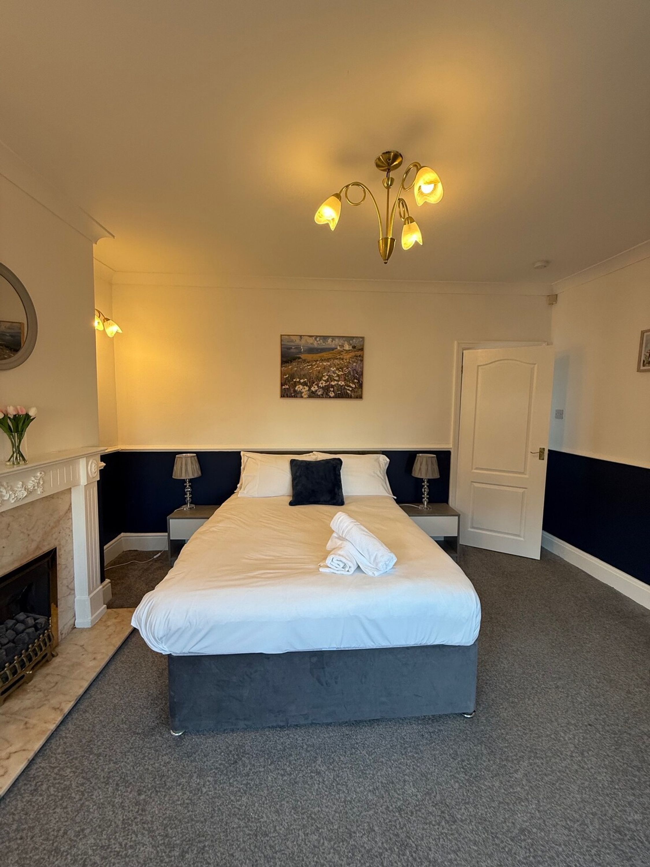 Una habitación de hotel con una cama grande, lámparas de noche, un cuadro en la pared y una puerta.