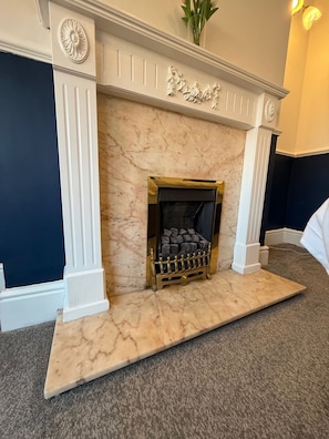 A marble fireplace with a gold-framed grate, flanked by white columns, and a decorative crest above. - Rochester House Horizon Stays (Middlesbrough)