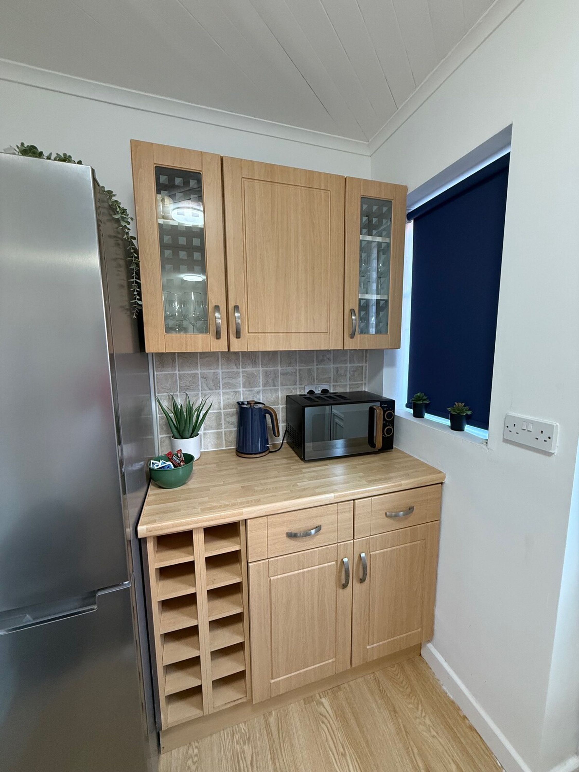 Una cocina compacta con muebles de madera, un microondas y una tetera.