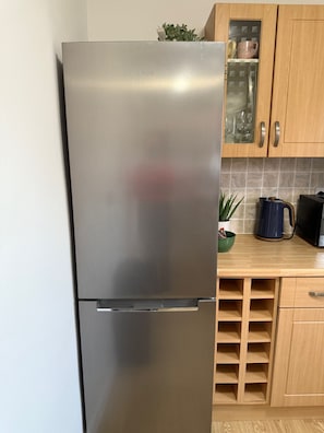 Ein Edelstahl-Kühlschrank in einer Küche mit Holzschränken und einer gefliesten Spritzschutzwand.