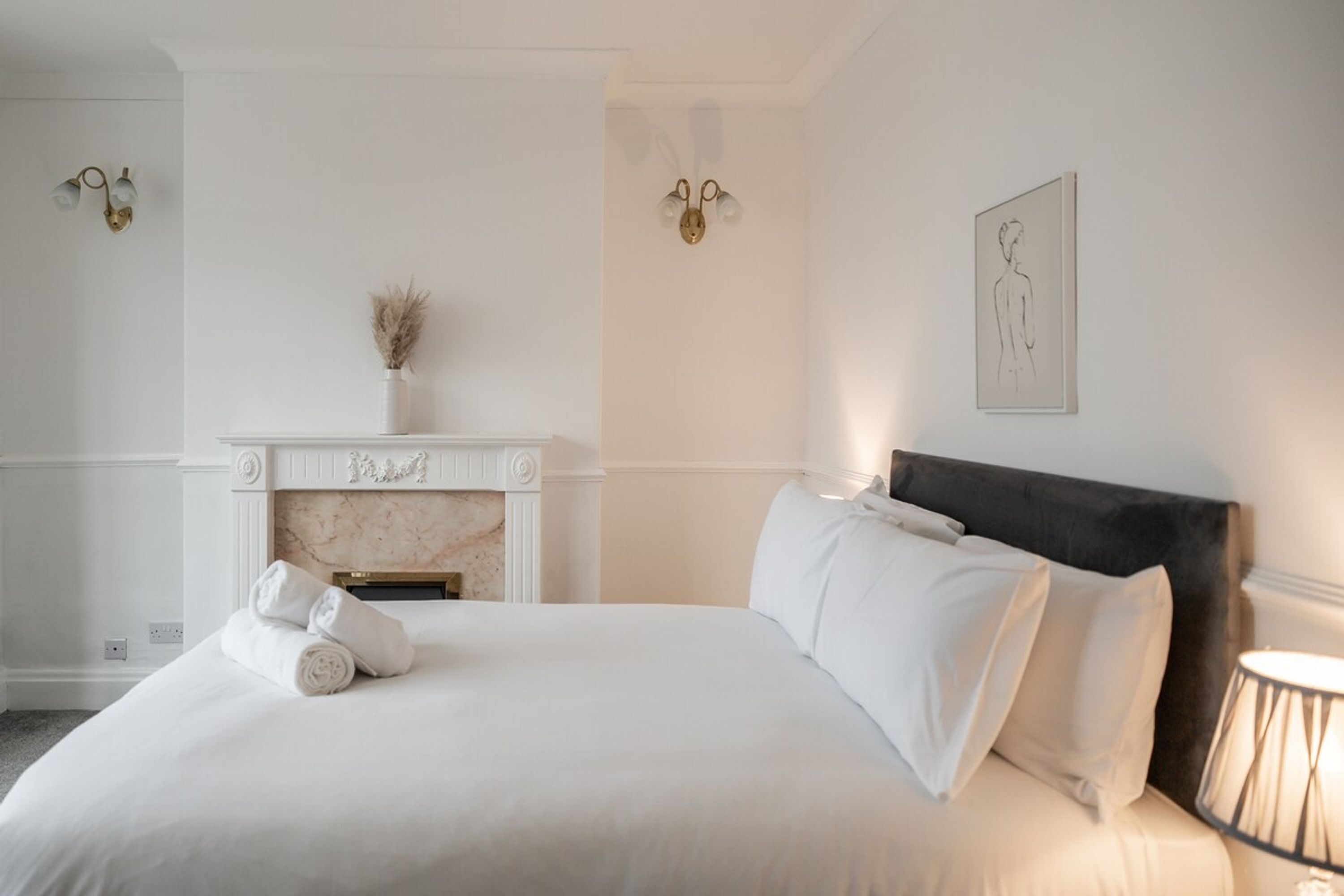 A hotel room with a bed, a fireplace, and a wall-mounted artwork.
