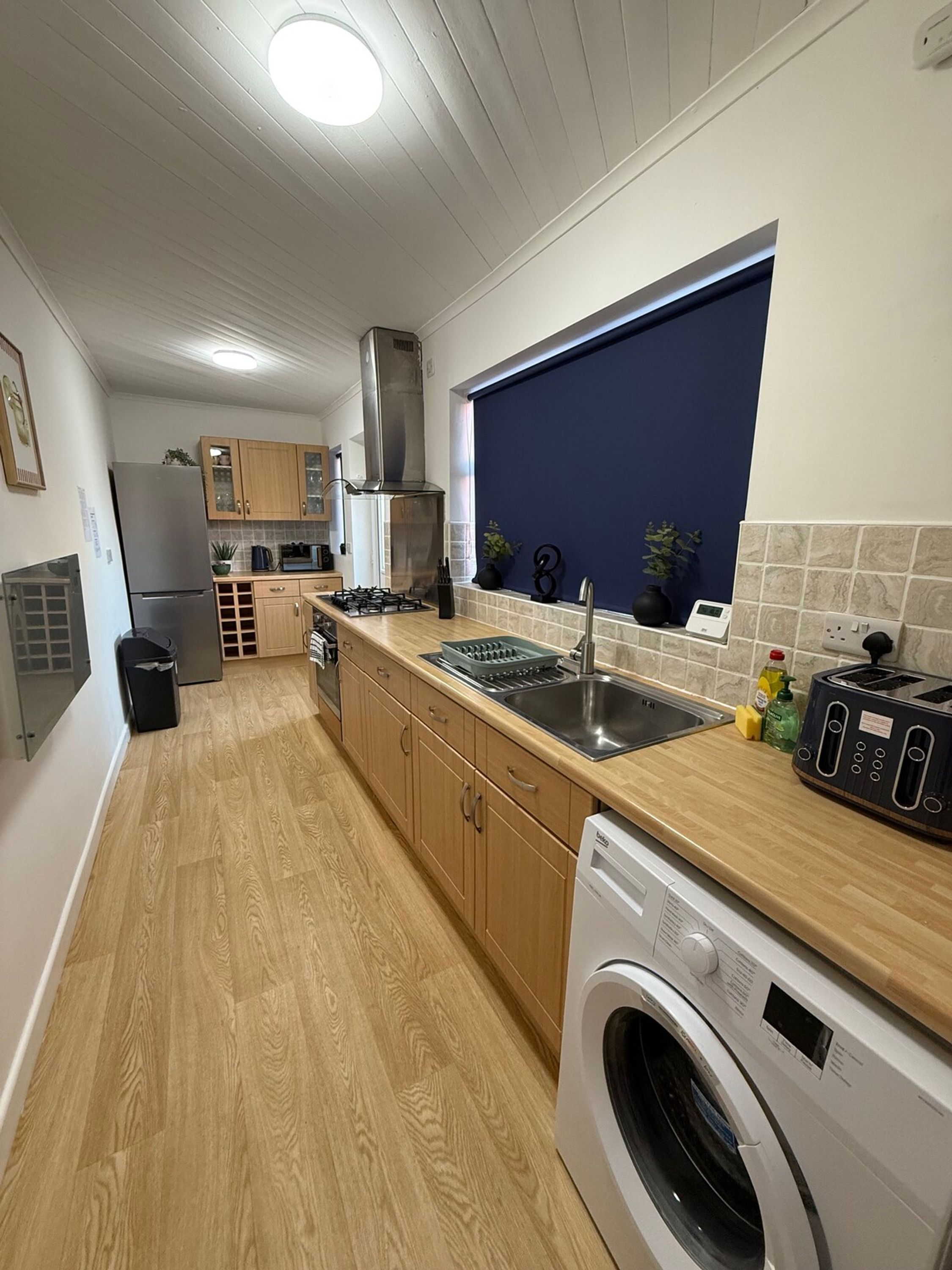 Une cuisine moderne avec des meubles en bois, un réfrigérateur en acier inoxydable, un four encastré, un lave-linge et une fenêtre avec vue.