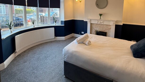 A hotel room with a curved window, a bed, a fireplace, and wall-mounted lighting. - Rochester House Horizon Stays (Middlesbrough)