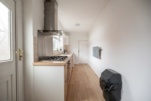 A narrow kitchen with a gas stove, a range hood, and a window. - Rochester House Horizon Stays (Middlesbrough)