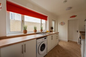 A modern kitchen with a washing machine, wooden countertop, and a red window blind. - The Blue Ember By Horizon Stays (Middlesbrough)
