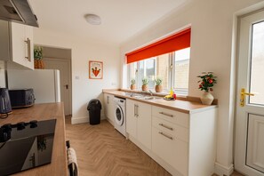 A compact kitchen with a washing machine, a sink, and a window with a red blind. - The Blue Ember By Horizon Stays (Middlesbrough)