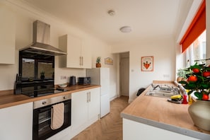 A modern kitchen with white cabinetry, a black stove, and a wooden countertop. - The Blue Ember By Horizon Stays (Middlesbrough)