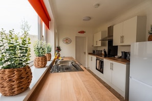 A modern kitchen with a wooden countertop, stainless steel appliances, and potted plants. - The Blue Ember By Horizon Stays (Middlesbrough)