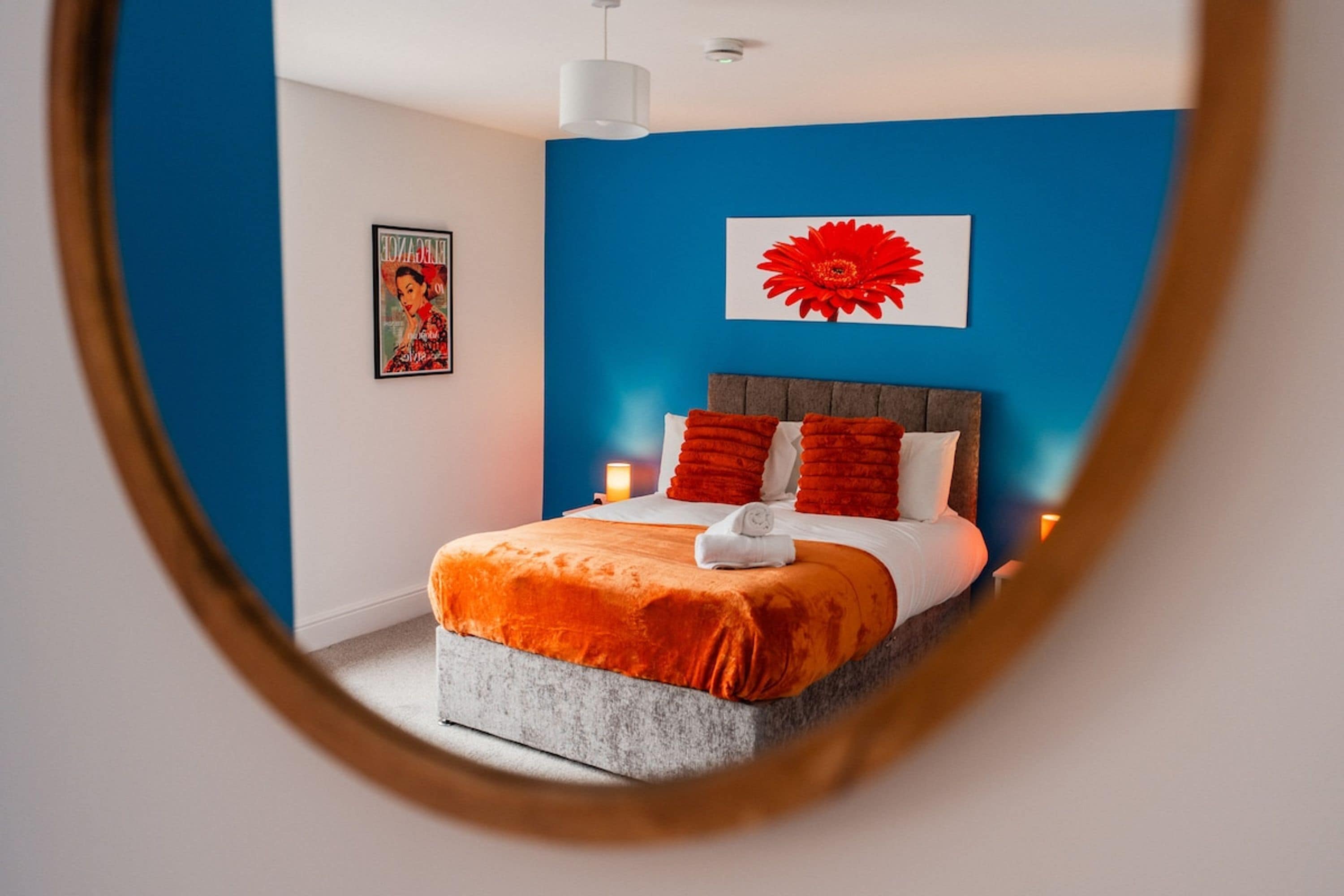 A bedroom with a bed, a wall-mounted artwork, and a bedside lamp.
