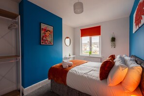 A bedroom with a bed, a window with a red blind, a wall-mounted mirror, and a poster. - The Blue Ember By Horizon Stays (Middlesbrough)
