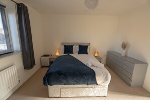 A bedroom with a bed, bedside tables, a dresser, a radiator, and a window with curtains. - Pottery Wharf Horizon Stays (Stockton-on-Tees)