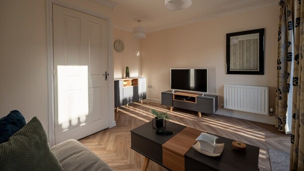 Ein modernes Wohnzimmer mit Sofa, Couchtisch, Fernseher und einem Essbereich mit Schrank.