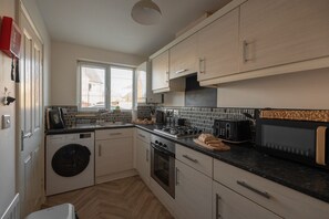 A compact kitchen with a washing machine, oven, and a microwave. - Pottery Wharf Horizon Stays (Stockton-on-Tees)