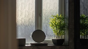 Ein Badezimmer mit Fenster, einem runden Spiegel und einer Topfpflanze.