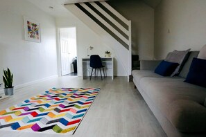 A modern living room with a chevron-patterned rug, a sofa with cushions, a desk with a chair, and a staircase. - Thornwood House Horizon Stays (Stockton-on-Tees)