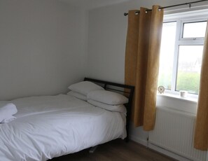 Ein Einzelbett mit weißer Bettwäsche in einem Zimmer mit Fenster und Heizkörper.