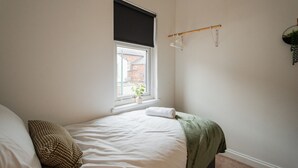 A bedroom with a single bed, a window with a view of a building, a hanging plant, and a towel on the bed. - The Alfred Suite Redcar (Redcar)