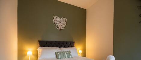 Un lit bien fait, avec du linge de lit blanc et un plaid vert, deux lampes de chevet et un élément décoratif mural au-dessus du lit.
