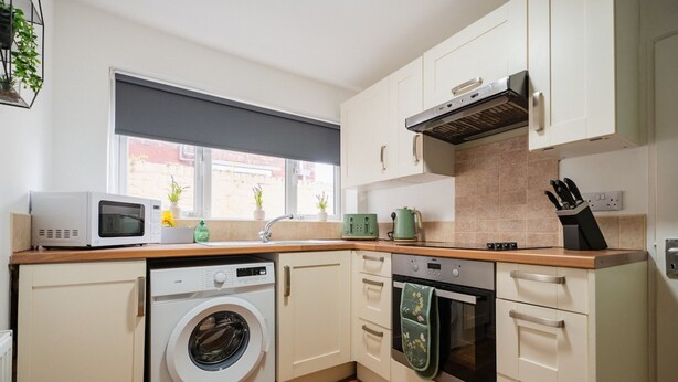 A compact kitchen with a washing machine, microwave, oven, and a window with a view of the street. - The Alfred Suite Redcar (Redcar)