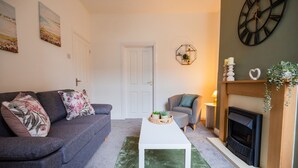 A living room with a grey sofa, a white coffee table, a fireplace, and a clock on the wall. - The Alfred Suite Redcar (Redcar)