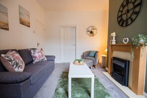 A living room with a grey sofa, a white coffee table, a fireplace, and a clock on the wall. - The Alfred Suite Redcar (Redcar)