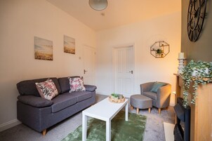 A living room with a grey sofa, a white coffee table, a grey armchair, and a decorative hexagonal wall piece.