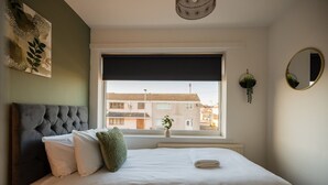 Ein Schlafzimmer mit einem großen Bett, einem Fenster mit Blick auf Gebäude, einem runden Spiegel und einer an der Wand befestigten Pflanze.