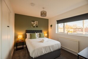 Ett hotellrum med en säng, två sänglampor, ett fönster med utsikt och en växt som hänger på väggen.