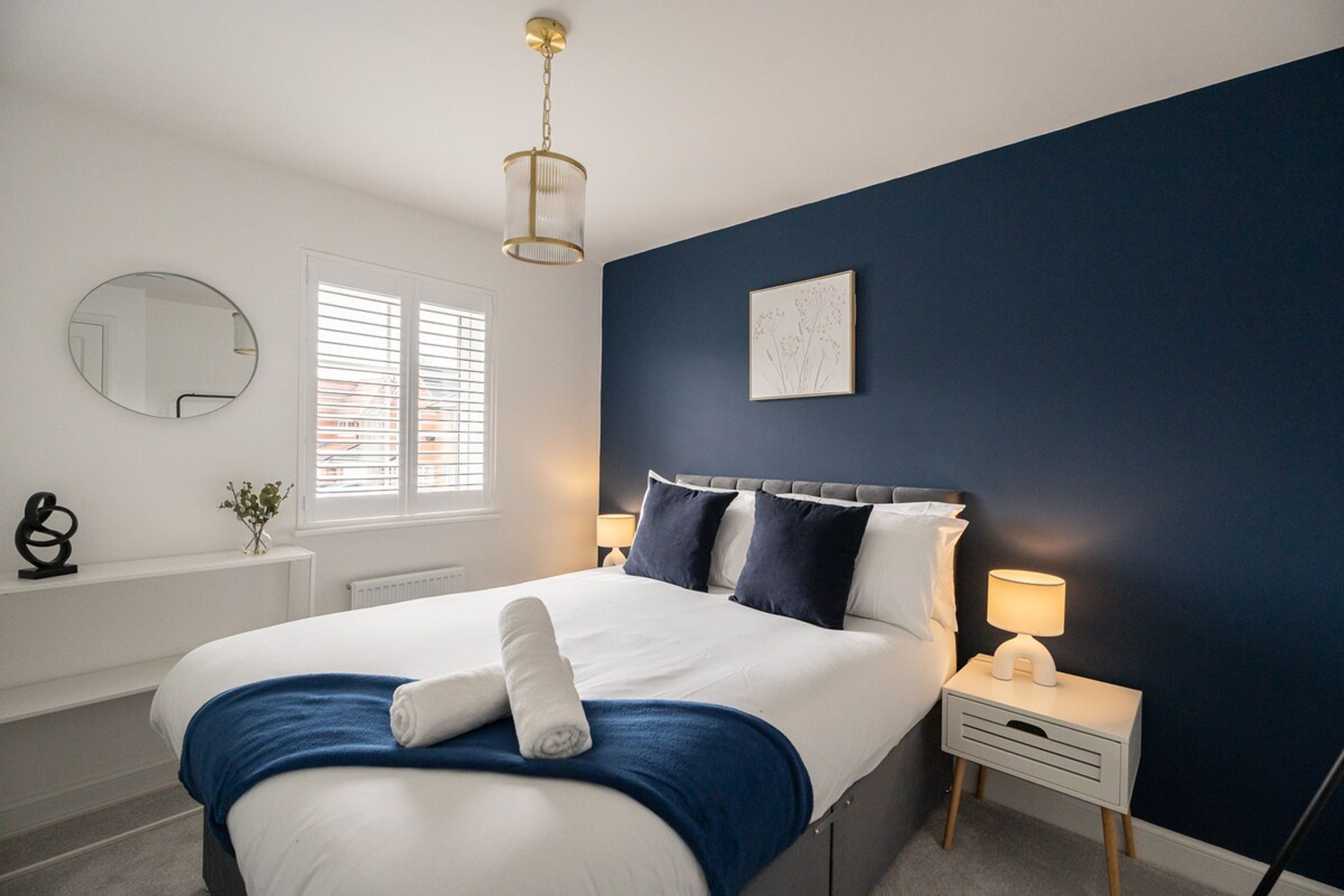 A bedroom with a bed, bedside tables, a mirror, and a window with blinds.