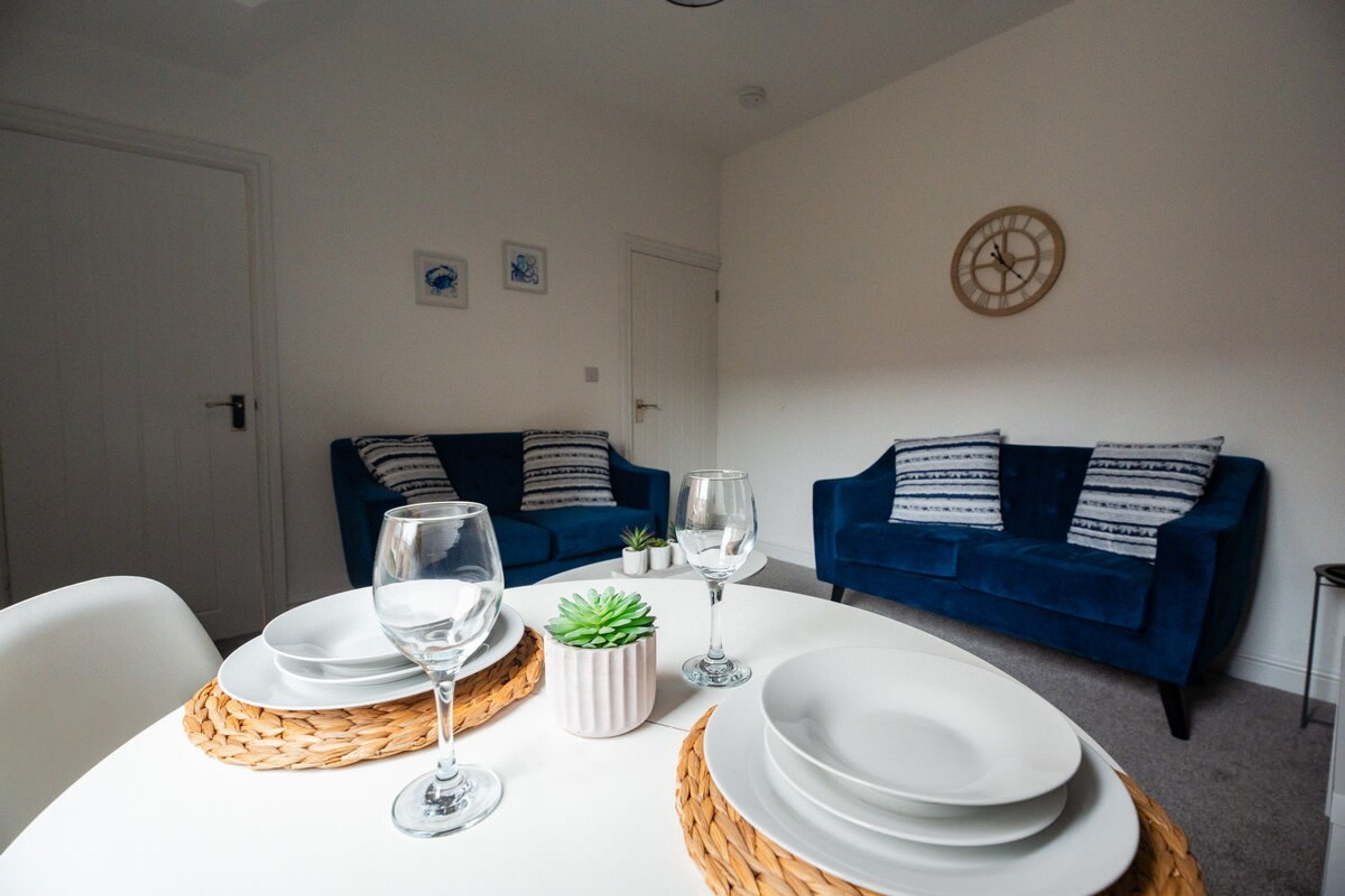 A dining area with a round table set for four, two blue sofas, and a wall clock.