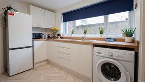Cocina compacta con lavadora integrada, refrigerador y ventana con persiana azul.