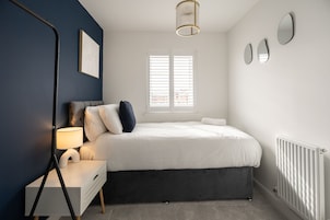 Un dormitorio con cama, mesita de noche, lámpara y ventana con persianas.