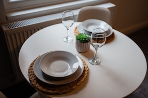 Una mesa dispuesta con platos, vasos y una pequeña planta en maceta, indicando un comedor.