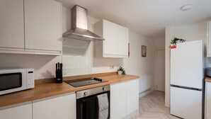 Una cocina moderna con gabinetes blancos, una campana extractora de acero inoxidable, microondas, horno empotrado y refrigerador.