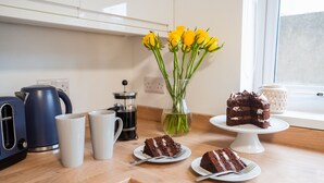 Una encimera de cocina con una cafetera, un pastel y un florero con flores amarillas.