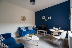 A living room with a blue sofa, a white coffee table, and a dining area with a white table and chairs.